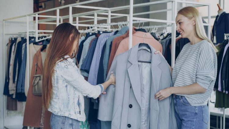 Two women shopping for jackets in a stylish clothing store, examining coats on a rack.