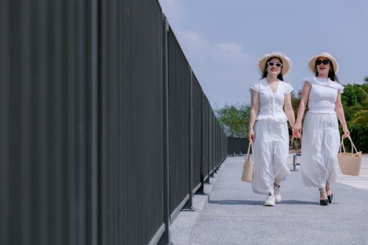 Two women in white summer outfits walking outdoors, enjoying a sunny day.