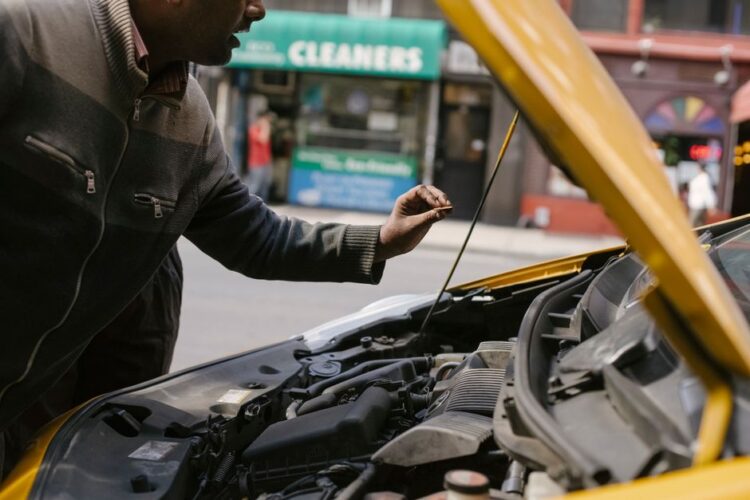 Side view of crop ethnic male repairing motor in broken auto parked on city street