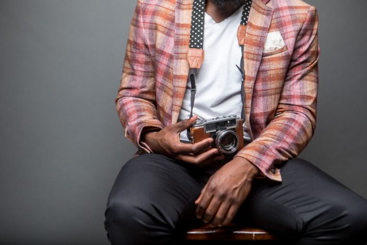Fashionable man sitting with a classic analog camera, showcasing modern style.