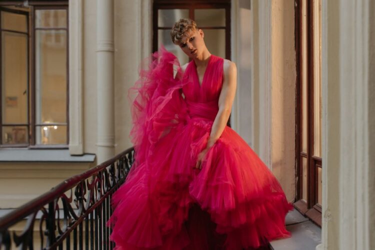 A fashionable man elegantly poses in a stunning pink gown on a balcony, showcasing contemporary style.